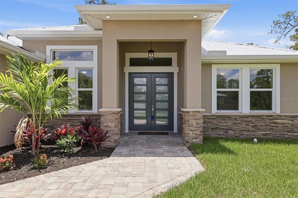 A modern house exterior features a stone-accented facade, double glass-paneled doors, and a paved walkway — 2649 SIMONTON AVENUE, NORTH PORT, FL
