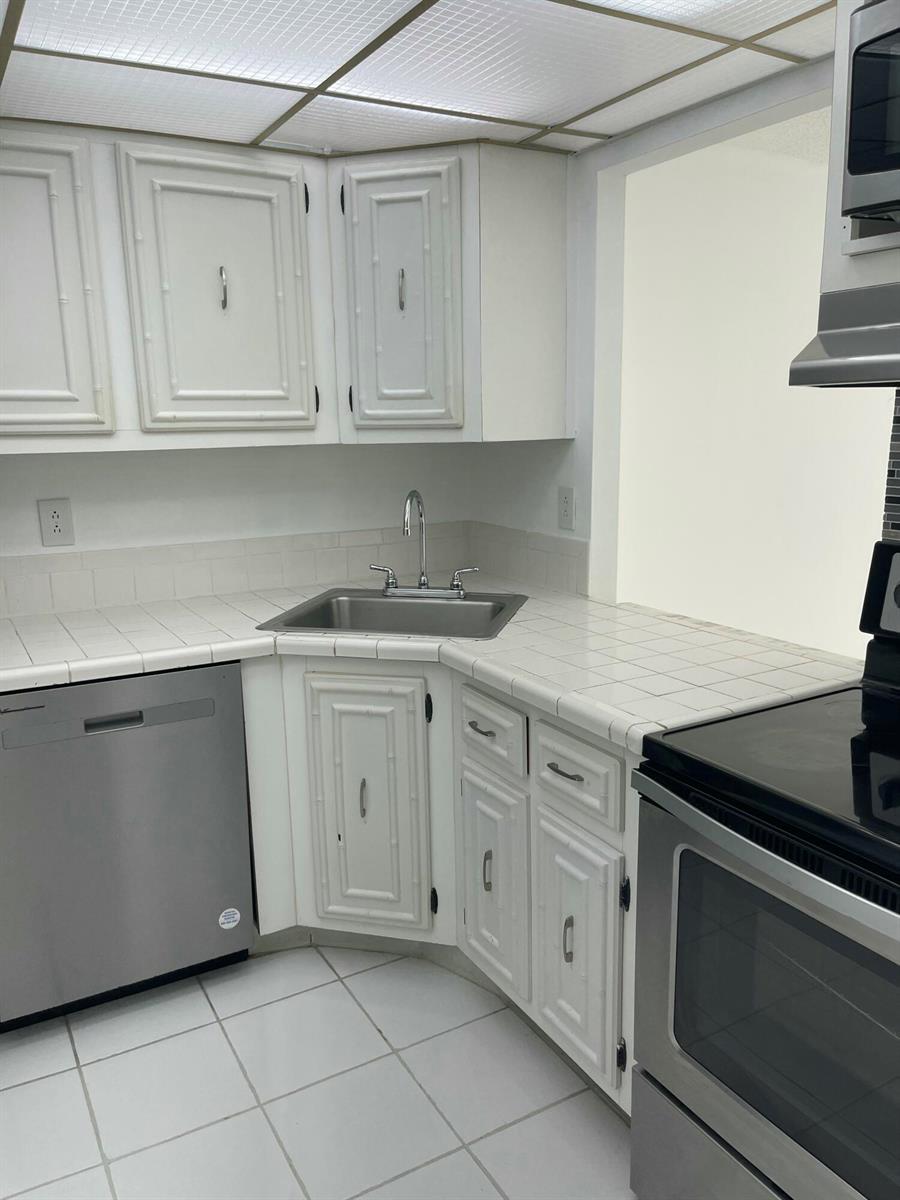 A kitchen features white cabinets, tiled countertops, a stainless steel sink, and stainless steel appliances — 801 Three Islands Boulevard # 306, Hallandale Beach FL 33009, HALLANDALE BEACH, FL