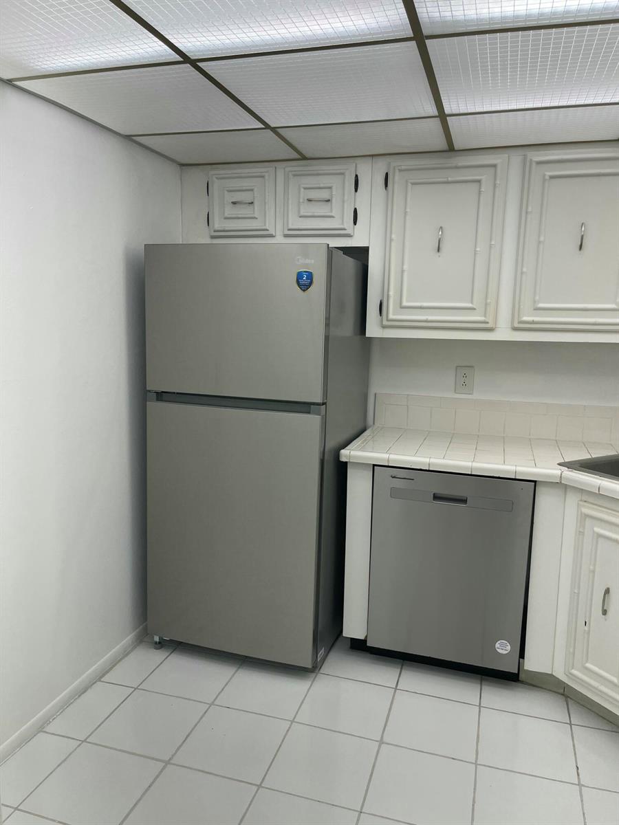 A kitchen features a stainless steel refrigerator, a dishwasher, white cabinets, and tiled flooring — 801 Three Islands Boulevard # 306, Hallandale Beach FL 33009, HALLANDALE BEACH, FL