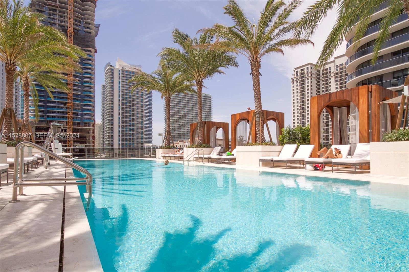 A rooftop swimming pool features lounge chairs, wooden cabanas, and palm trees against city skyscrapers — 801 S Miami Ave # 3009, Miami FL 33130, MIAMI, FL