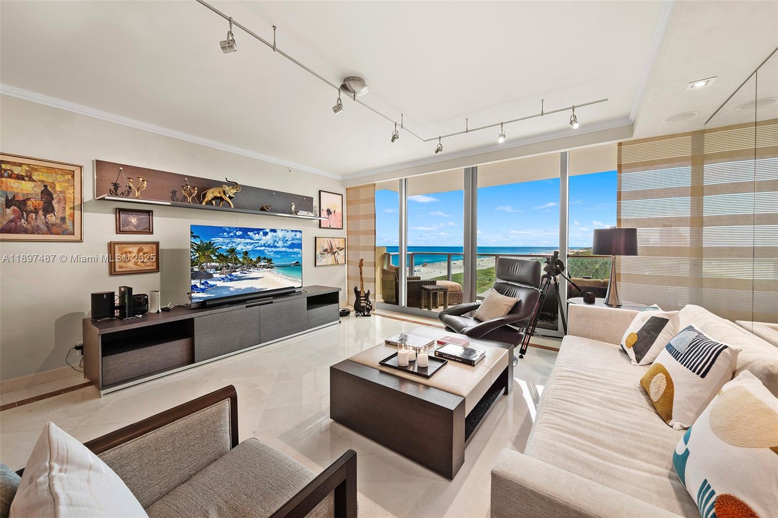 A modern living room features a large television, neutral furniture, and floor-to-ceiling ocean views — 1455 Ocean Dr # 1003, Miami Beach FL 33139, MIAMI BEACH, FL