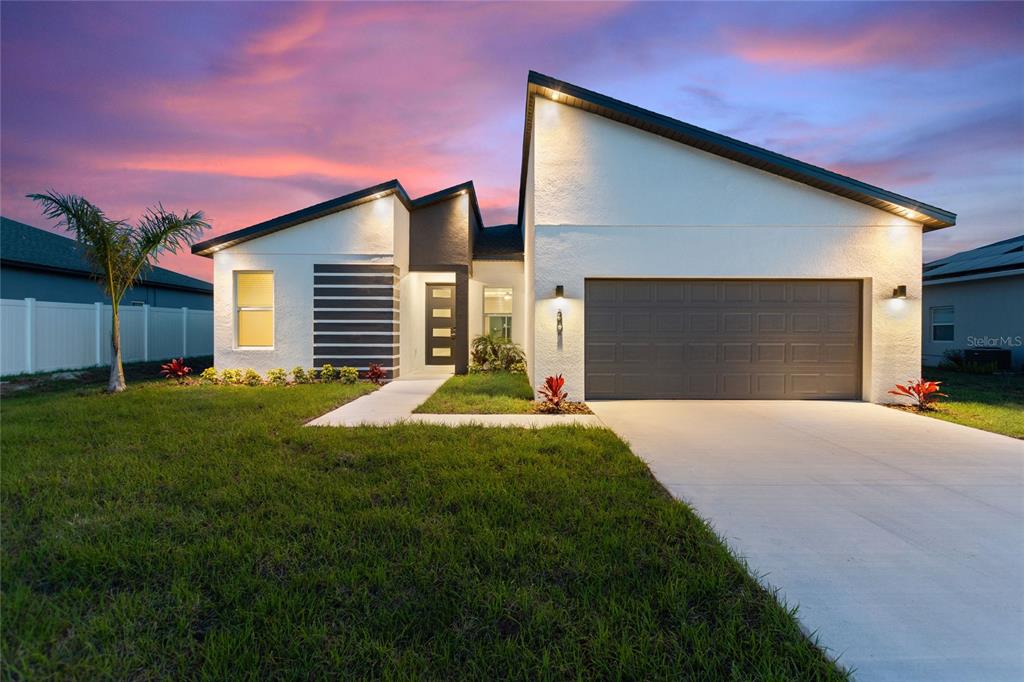 A modern single-story house with a white stucco exterior and a two-car garage at sunset — 302 ELDERBERRY COURT, KISSIMMEE, FL
