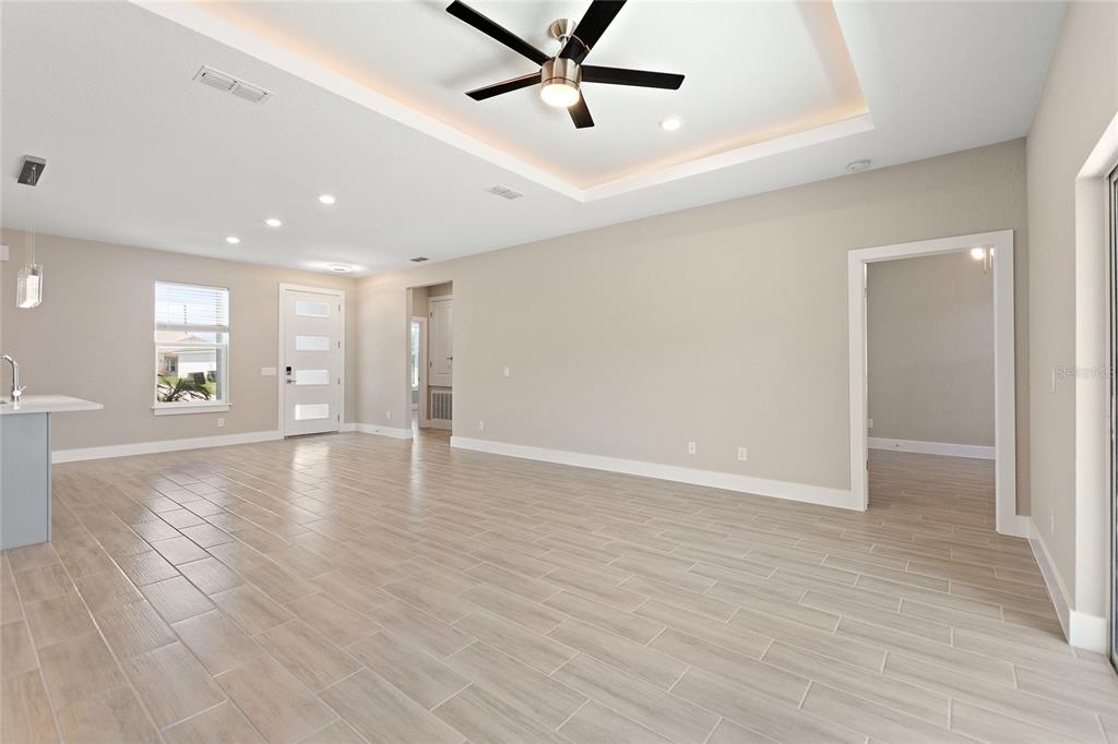 An open-concept living area features light wood-look tile flooring, a tray ceiling, and recessed lighting — 302 ELDERBERRY COURT, KISSIMMEE, FL