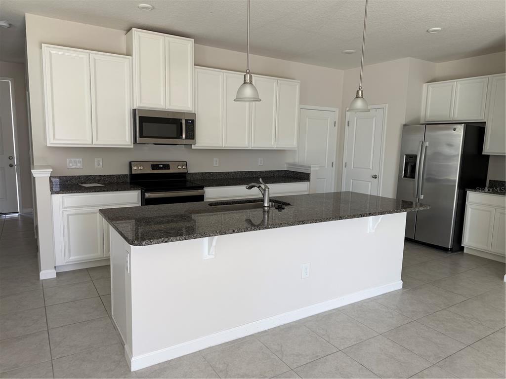 A kitchen features white cabinets, granite countertops, stainless steel appliances, and a central island — 2670 PLEASANT CYPRESS CIRCLE, KISSIMMEE, FL