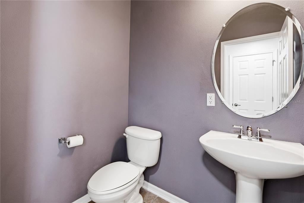A half bathroom features a pedestal sink, a toilet, and a round wall mirror — 6364 LAKE SMITH CIRCLE, WINDERMERE, FL