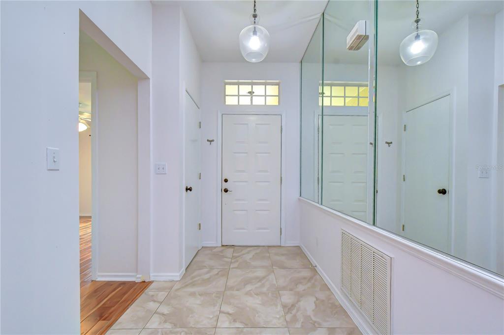 An entryway features tiled flooring, a white front door, and a large mirrored wall — 818 MCCALLISTER AVENUE, SUN CITY CENTER, FL