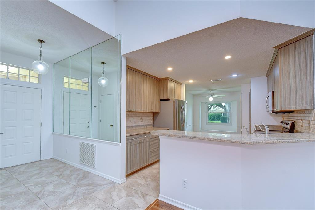 A kitchen with light wood cabinets, granite countertops, and a mirrored wall near the entrance — 818 MCCALLISTER AVENUE, SUN CITY CENTER, FL