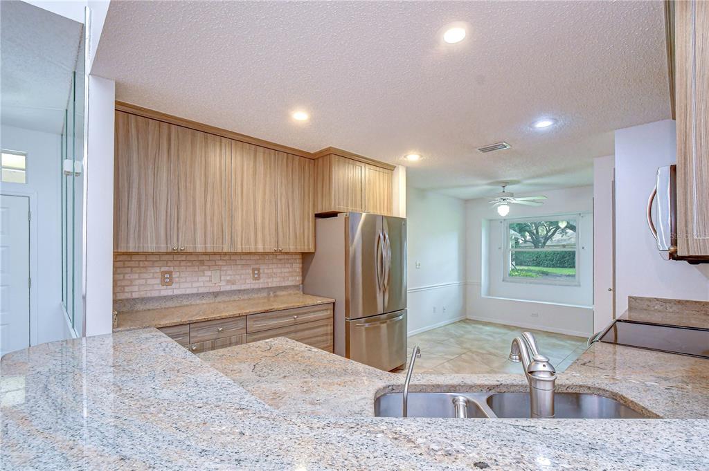 A kitchen features light wood cabinets, granite countertops, stainless steel appliances, and a breakfast nook — 818 MCCALLISTER AVENUE, SUN CITY CENTER, FL