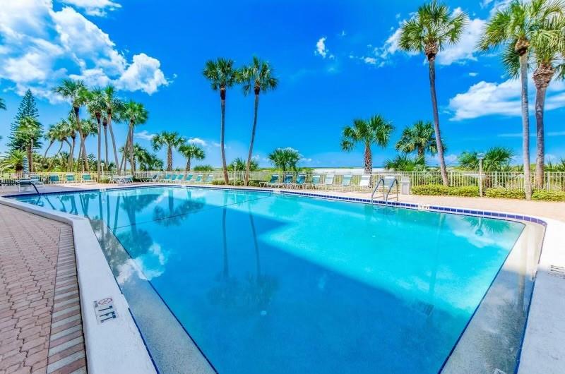 A swimming pool with palm trees and lounge chairs under a clear blue sky — 1270 GULF BOULEVARD UNIT 1501, CLEARWATER BEACH, FL