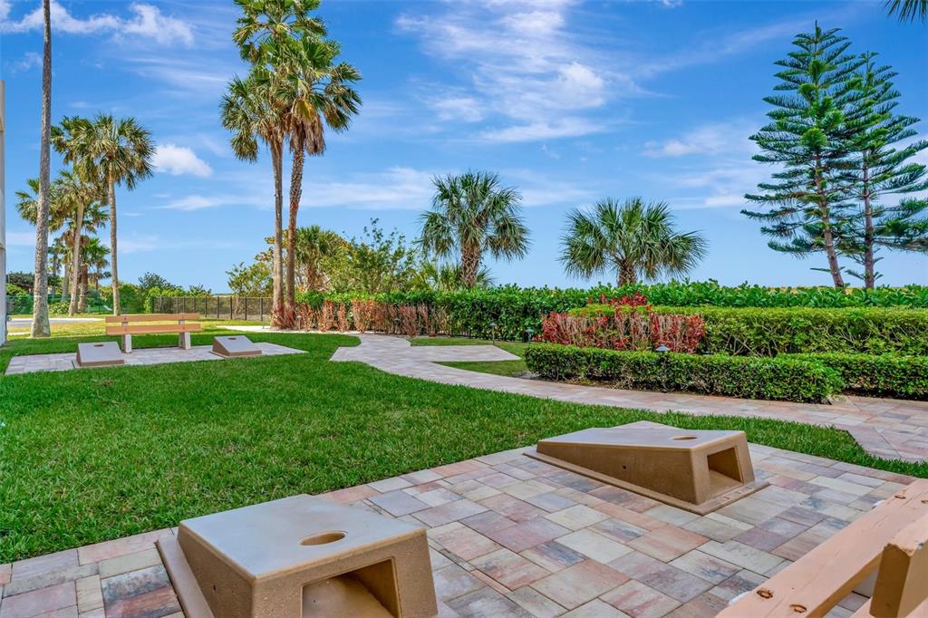 An outdoor patio area features cornhole boards, a wooden bench, and lush tropical landscaping — 1270 GULF BOULEVARD UNIT 1501, CLEARWATER BEACH, FL