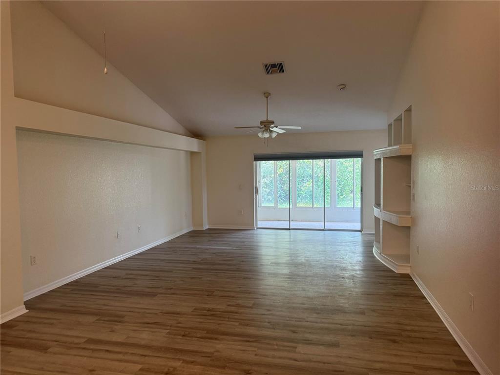 A spacious living room features vaulted ceilings, wood-look flooring, built-in shelving, and sliding glass doors — 9443 BURNAM DRIVE, WEEKI WACHEE, FL