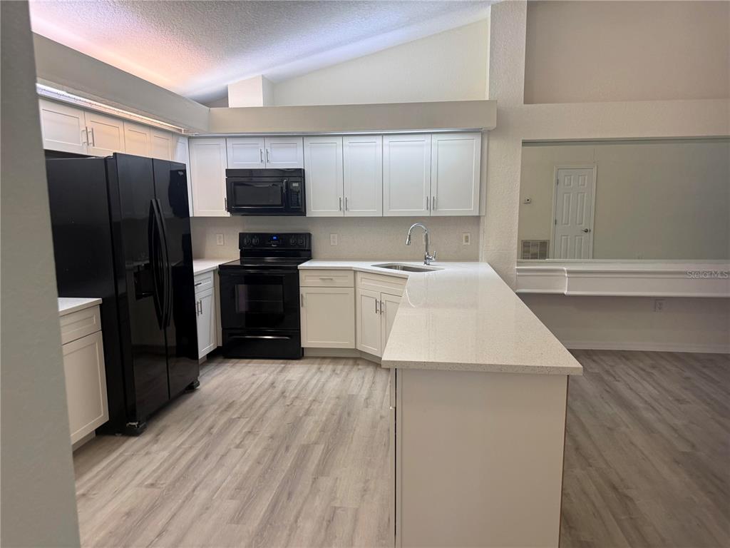 A kitchen features white cabinets, black appliances, a quartz countertop, and light wood-look flooring — 9443 BURNAM DRIVE, WEEKI WACHEE, FL