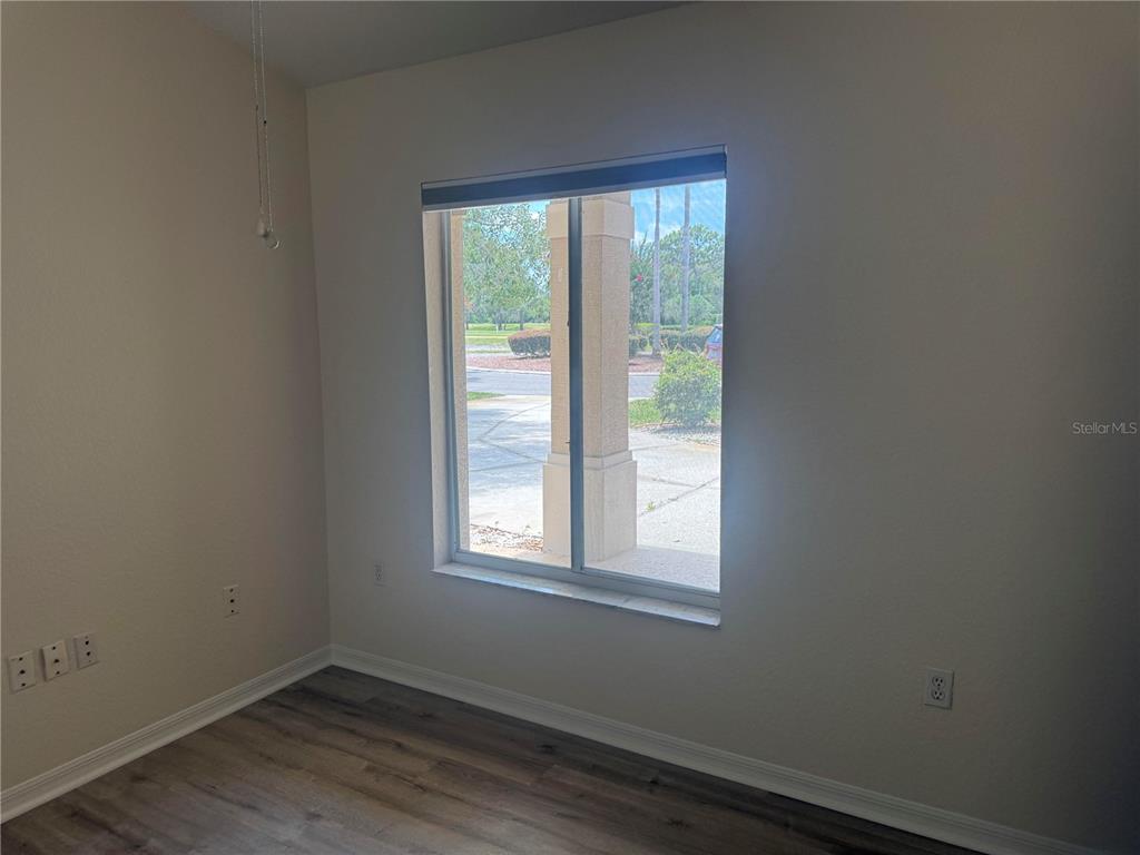 An empty room features wood-look flooring, beige walls, and a window overlooking a driveway — 9443 BURNAM DRIVE, WEEKI WACHEE, FL