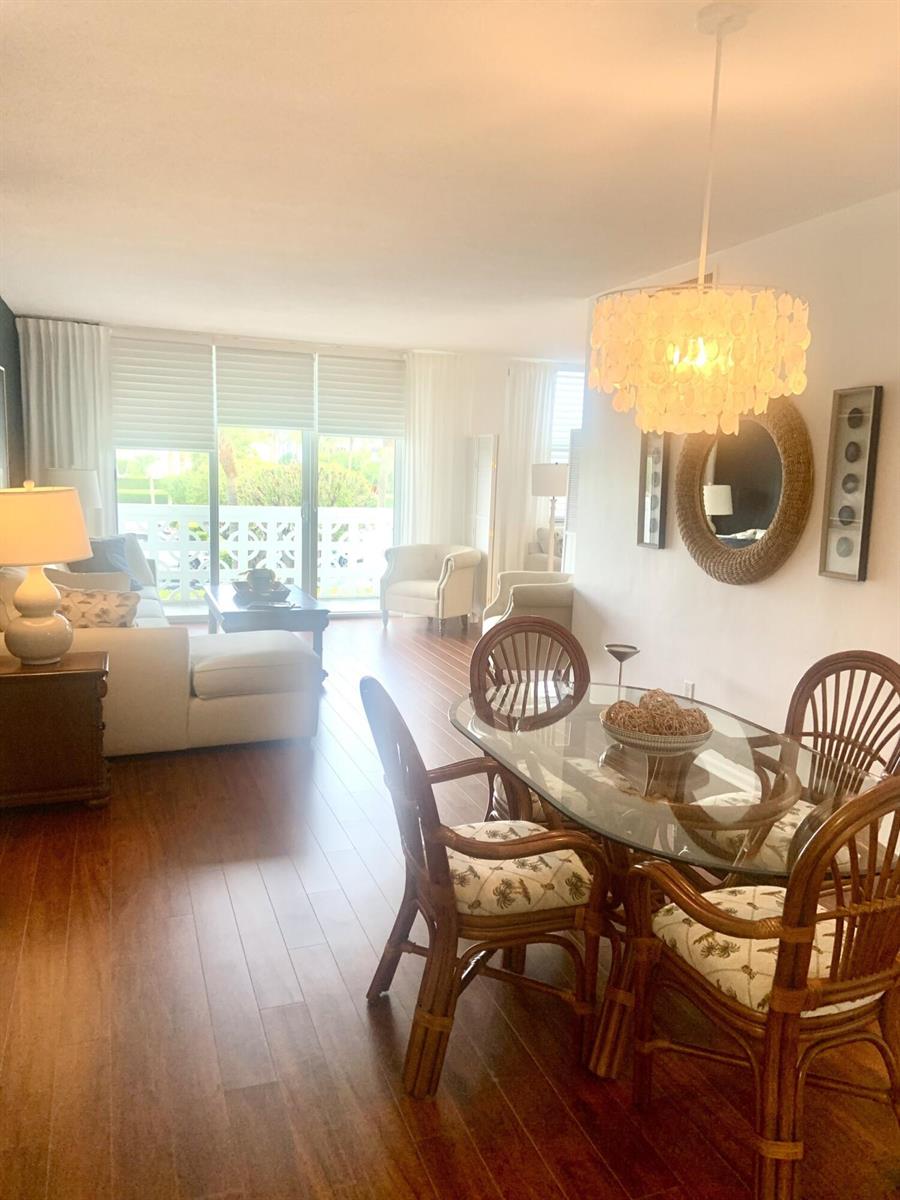 A dining area with a glass table and rattan chairs sits before a bright living room — 2840 S Ocean Boulevard # 2050, Palm Beach FL 33480, PALM BEACH, FL