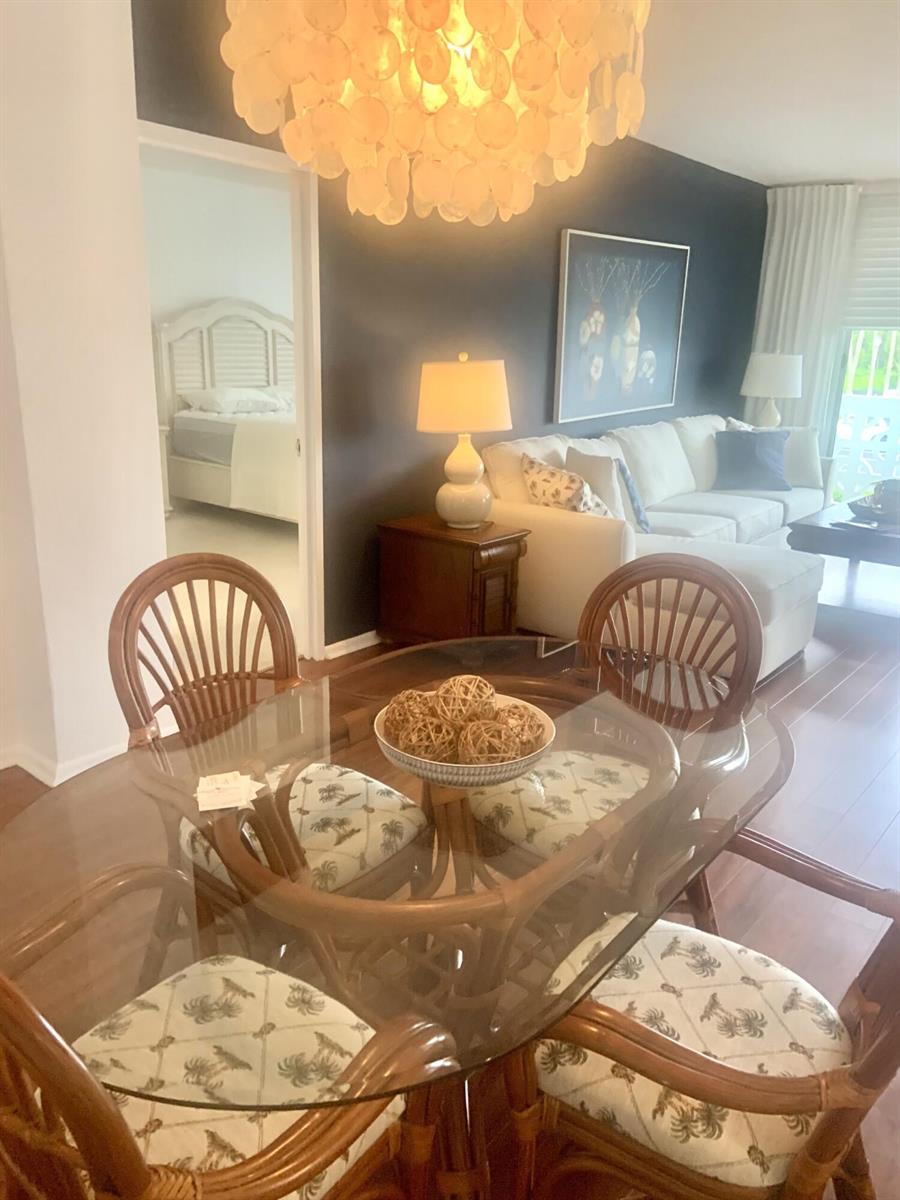 A dining area with a glass table and rattan chairs overlooks a living room — 2840 S Ocean Boulevard # 2050, Palm Beach FL 33480, PALM BEACH, FL