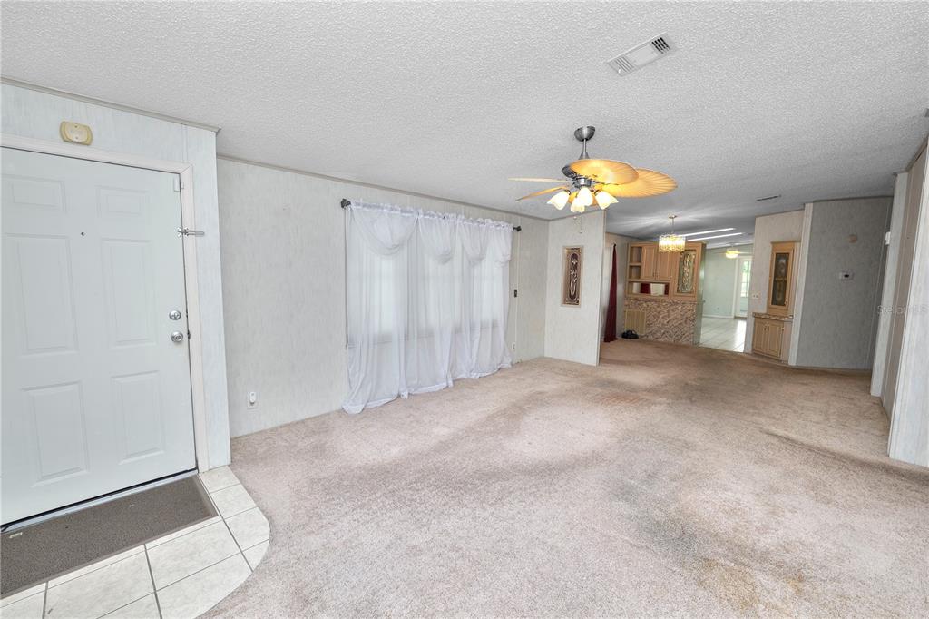 A living room with beige carpet, white paneled walls, a ceiling fan, and a front door — 3562 LAZY LAKE DRIVE N, LAKELAND, FL