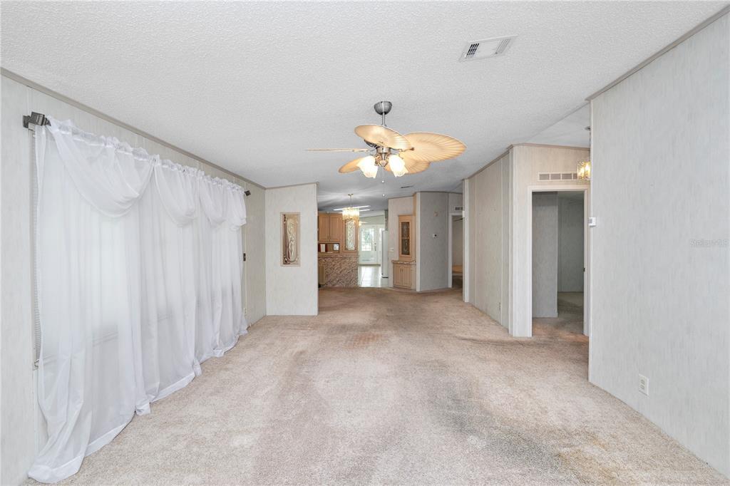 A living room with beige carpet, white paneled walls, and a ceiling fan — 3562 LAZY LAKE DRIVE N, LAKELAND, FL