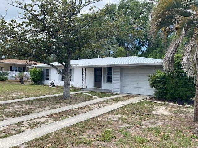 A single-story white house with a metal roof, attached garage, and a large front tree — 6442 TREEHAVEN DRIVE, SPRING HILL, FL