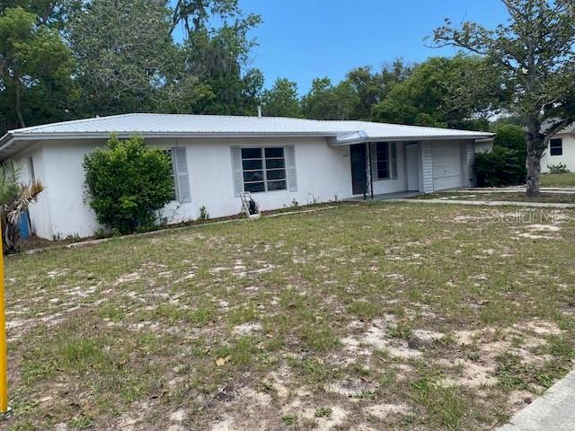 A single-story white house with a metal roof sits on a grassy lot — 6442 TREEHAVEN DRIVE, SPRING HILL, FL