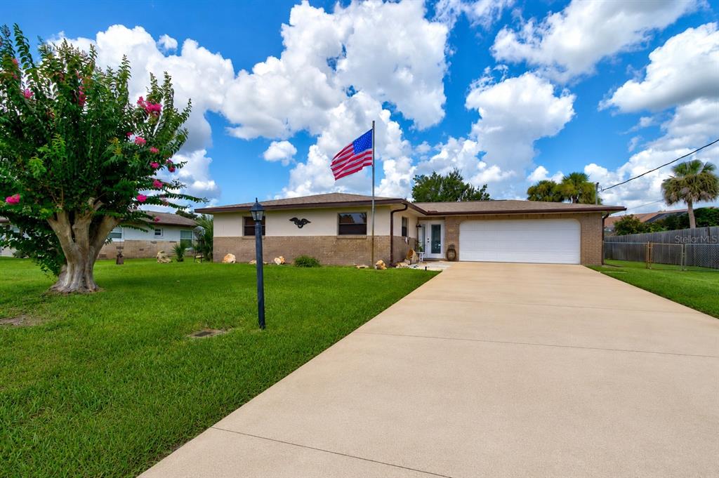 A single-story brick house with a large driveway, a front lawn, and an American flag — 103 DEE STREET, NEW SMYRNA BEACH, FL