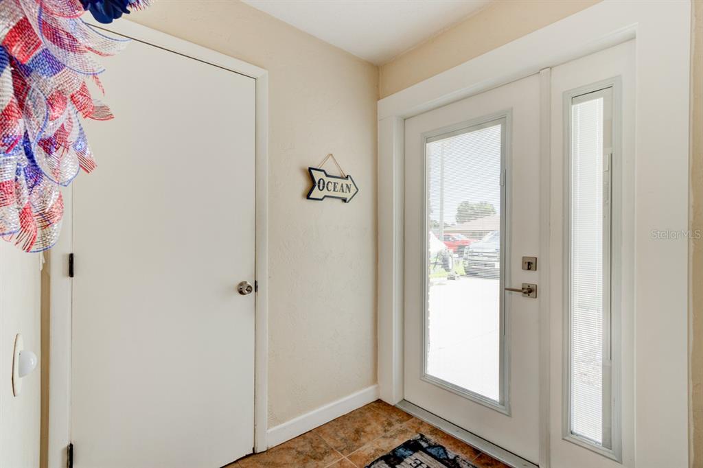An entryway features a white door, a side light, tile flooring, and an ocean sign — 103 DEE STREET, NEW SMYRNA BEACH, FL