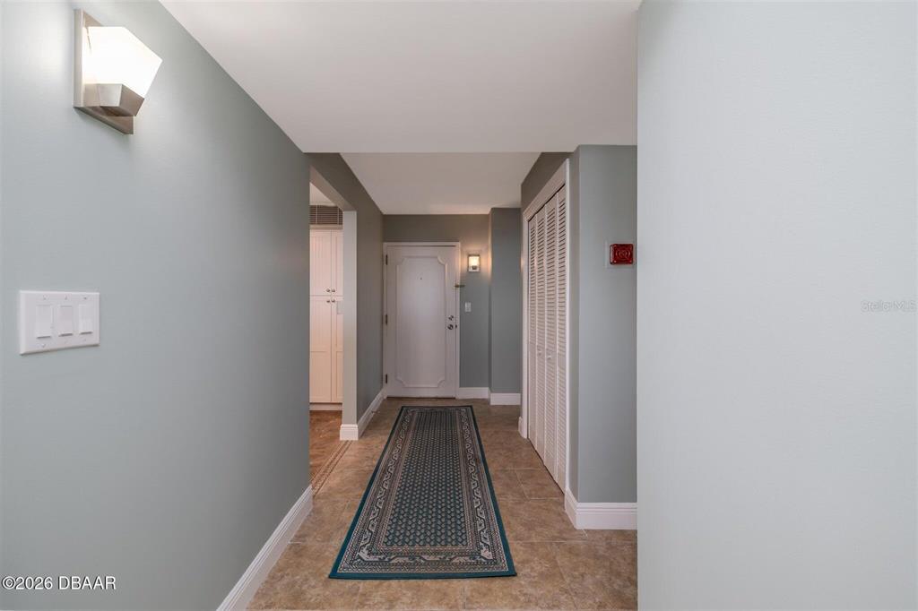 A hallway features light blue walls, tile flooring, a runner rug, and a white door — 1420 N ATLANTIC AVENUE UNIT 1601, DAYTONA BEACH, FL
