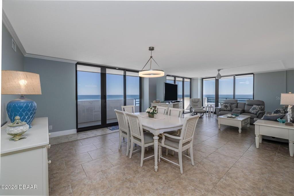 An open-concept living and dining area features tile flooring, white furniture, and floor-to-ceiling ocean views — 1420 N ATLANTIC AVENUE UNIT 1601, DAYTONA BEACH, FL