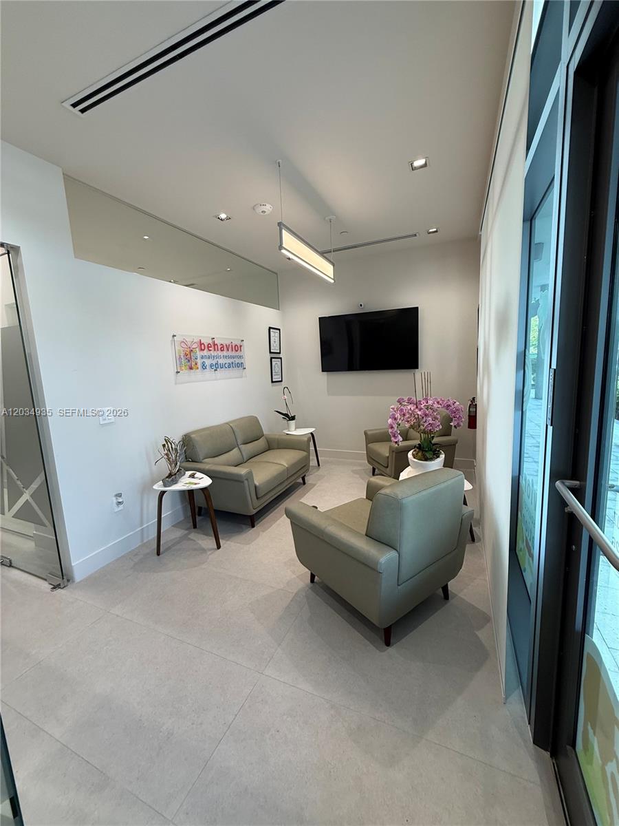 A modern waiting room features light gray leather seating, a wall-mounted television, and tile flooring — SWEETWATER, FL