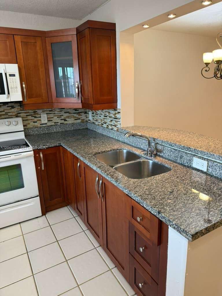 A kitchen features wood cabinets, granite countertops, a double sink, and white tile flooring — 8610 N Sherman Cir # 508, Miramar FL 33025, MIRAMAR, FL