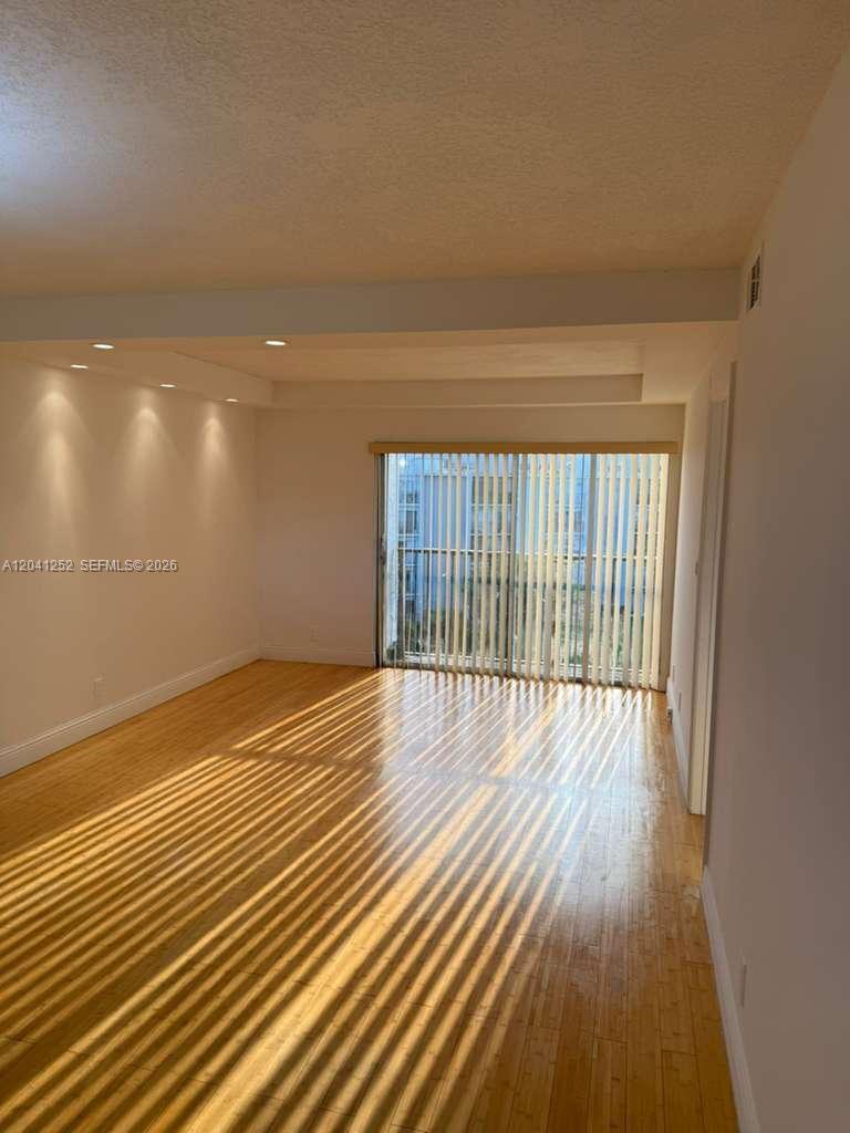 An empty room features light wood flooring, recessed lighting, and vertical blinds covering a balcony door — 8610 N Sherman Cir # 508, Miramar FL 33025, MIRAMAR, FL