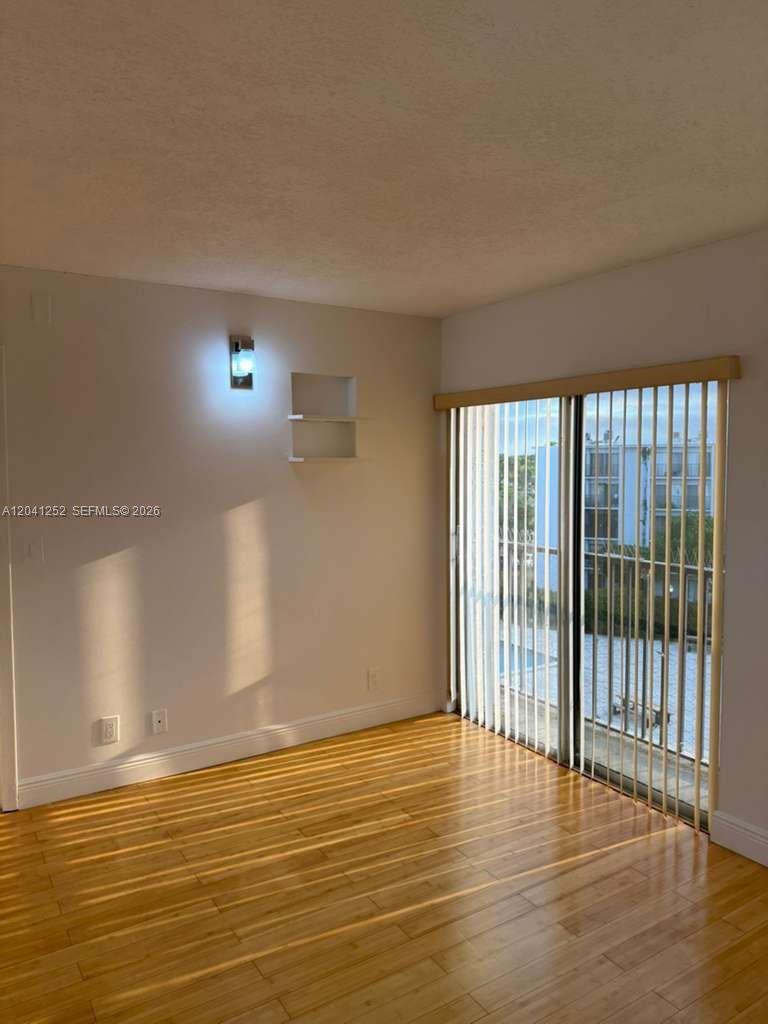 An empty room with light wood flooring, a wall-mounted light, shelves, and vertical blinds — 8610 N Sherman Cir # 508, Miramar FL 33025, MIRAMAR, FL