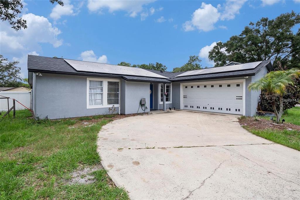 A single-story house with a gray exterior, solar panels on the roof, and a concrete driveway — 15906 COUNTRY FARM PLACE, TAMPA, FL