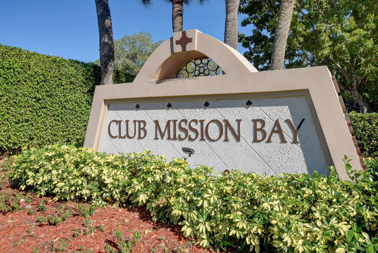 A beige stucco monument sign for Club Mission Bay sits behind a landscaped garden bed — 11038 Baybreeze Way, Boca Raton FL 33428, BOCA RATON, FL