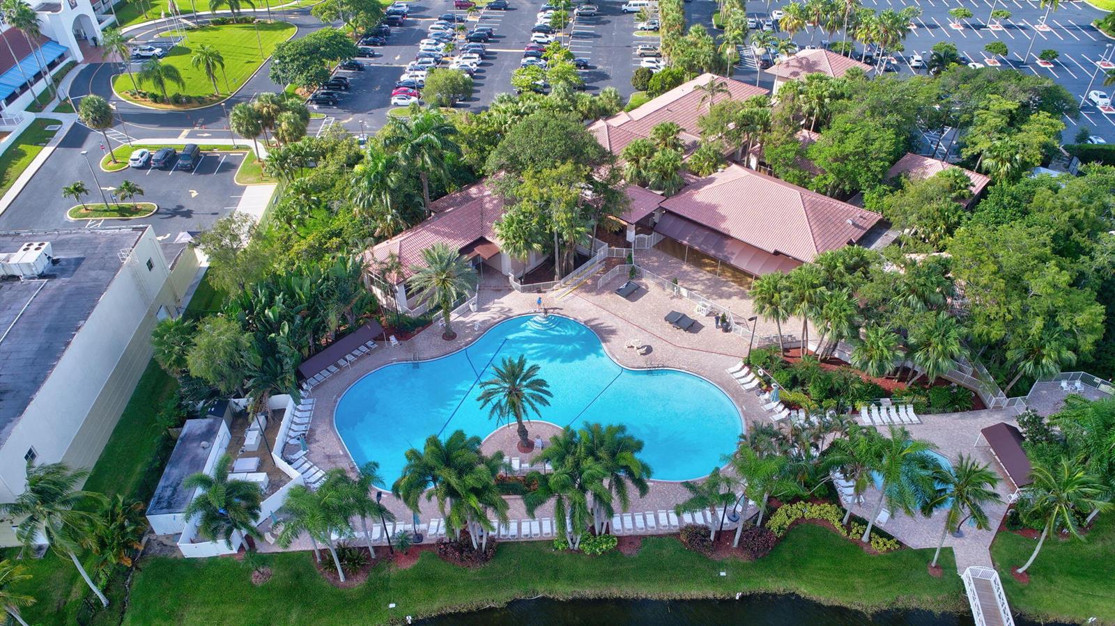 An aerial view shows a resort-style swimming pool surrounded by palm trees and building structures — 11038 Baybreeze Way, Boca Raton FL 33428, BOCA RATON, FL