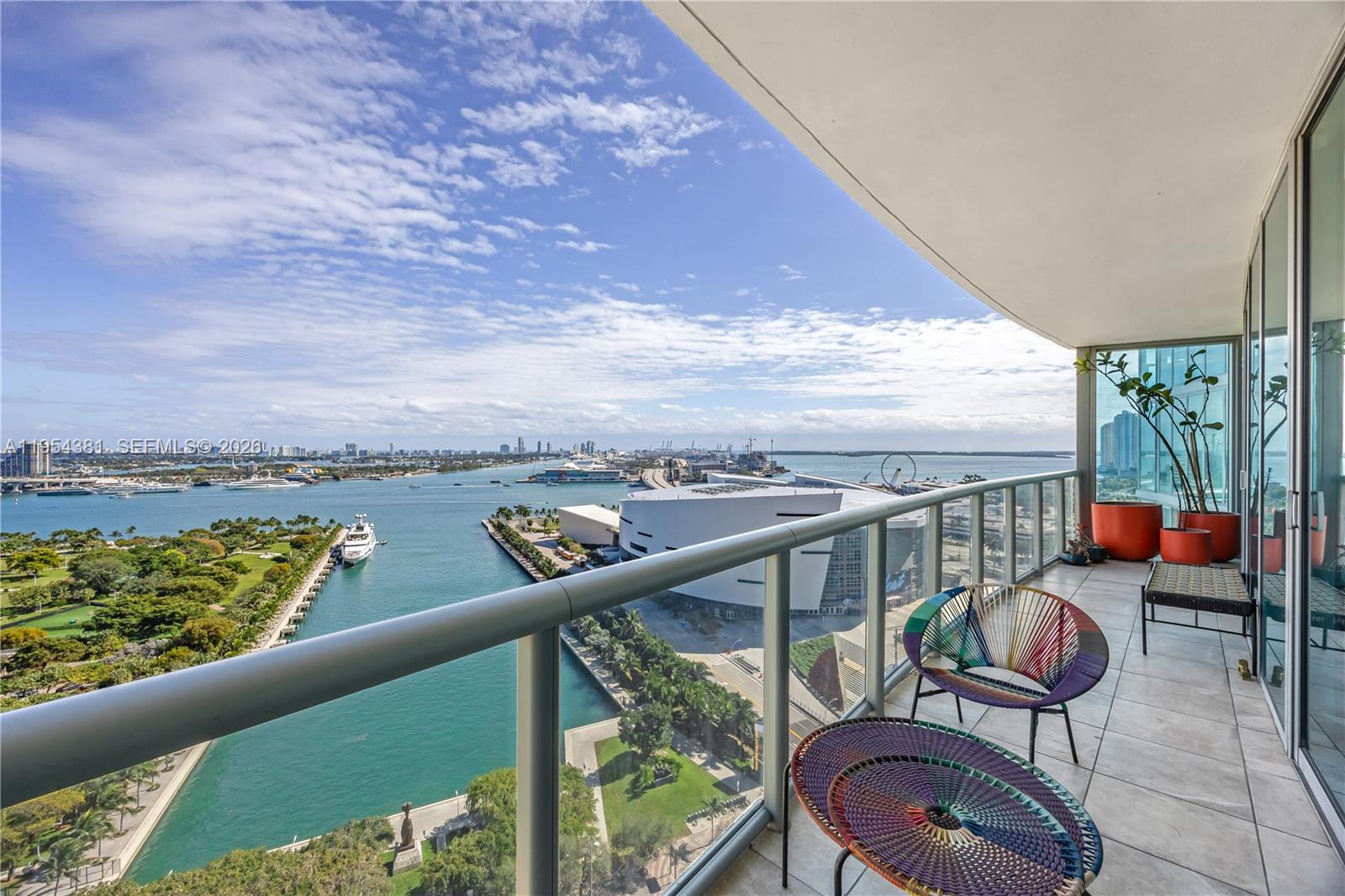 A balcony with colorful woven furniture overlooks a bay, a park, and a city skyline — 888 Biscayne Blvd # 2009, Miami FL 33132, MIAMI, FL