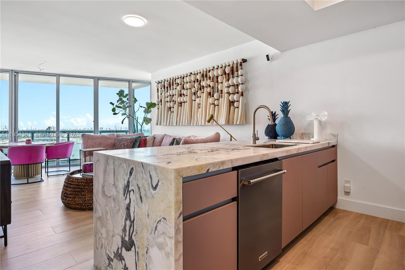 A kitchen island with a marble waterfall countertop sits in a room with pink cabinetry — 888 Biscayne Blvd # 2009, Miami FL 33132, MIAMI, FL