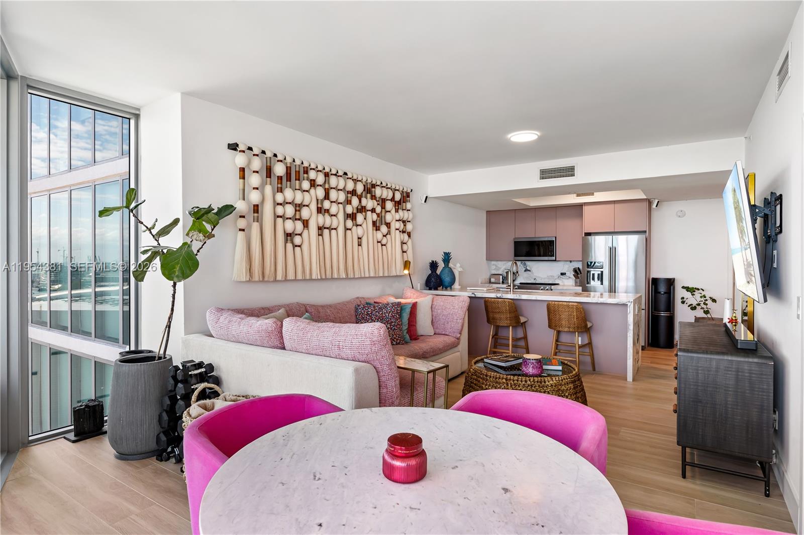 A living room and kitchen area features a pink sofa, dining table, and floor-to-ceiling windows — 888 Biscayne Blvd # 2009, Miami FL 33132, MIAMI, FL