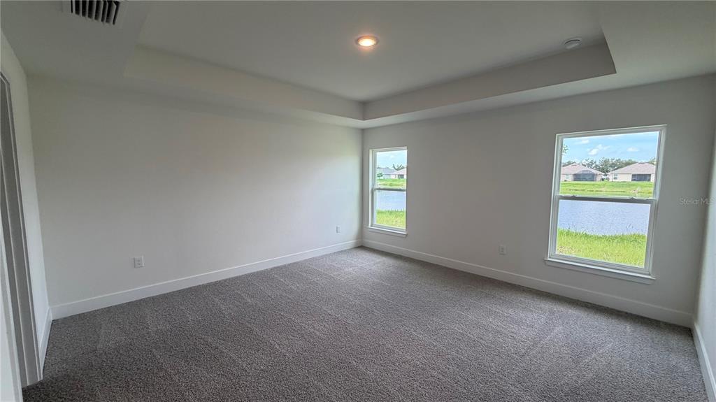 An empty bedroom with gray carpet, a tray ceiling, and windows overlooking a pond — 2683 AVERLAND LOOP, NORTH PORT, FL