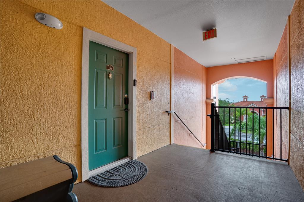 A green apartment door with a welcome mat sits on an outdoor concrete landing — 2705 VIA MURANO UNIT 131, CLEARWATER, FL