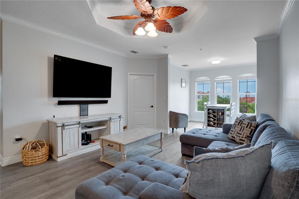 A living room features a gray sectional sofa, a white media console, and a ceiling fan — 2705 VIA MURANO UNIT 131, CLEARWATER, FL