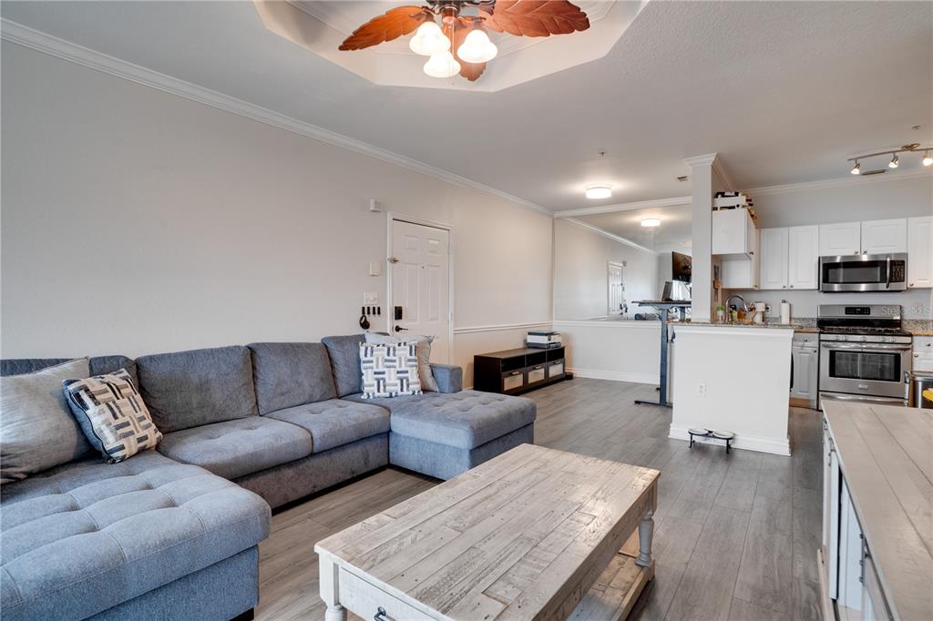 A living room with a grey sectional sofa, wooden coffee table, and an adjacent kitchen — 2705 VIA MURANO UNIT 131, CLEARWATER, FL