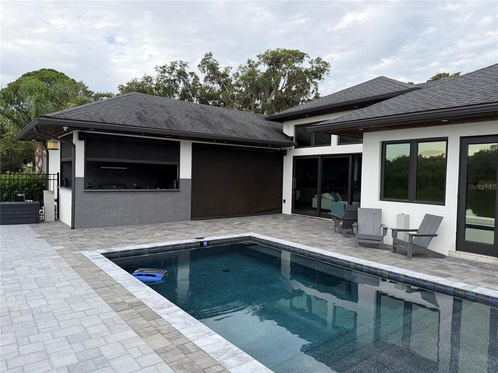 A swimming pool sits on a paved patio beside a house with an outdoor kitchen — 995 STACY LANE, NEW SMYRNA BEACH, FL