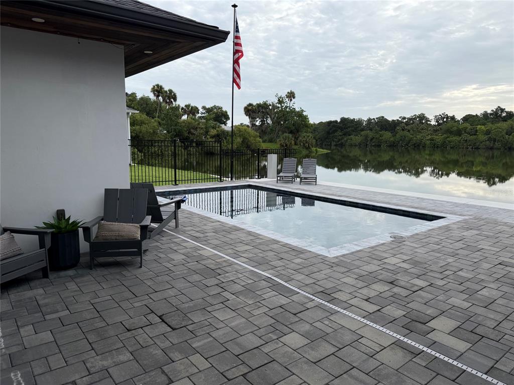 A patio with a rectangular pool overlooks a lake under a cloudy sky — 995 STACY LANE, NEW SMYRNA BEACH, FL