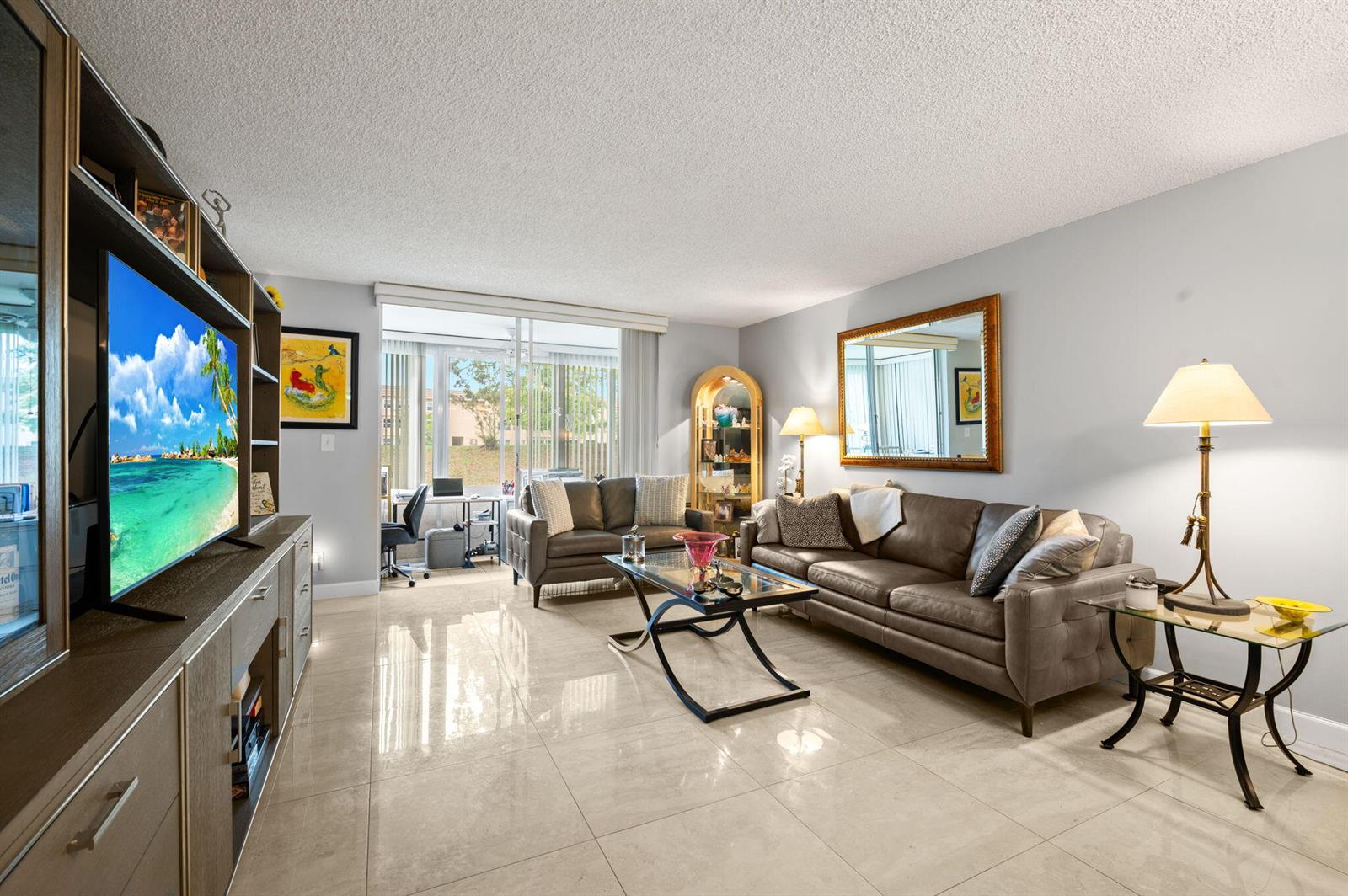 A living room features a brown leather sofa, glass coffee table, and large wall mirror — 9330 E Sunrise Lakes Boulevard E # 104, Sunrise FL 33322, SUNRISE, FL