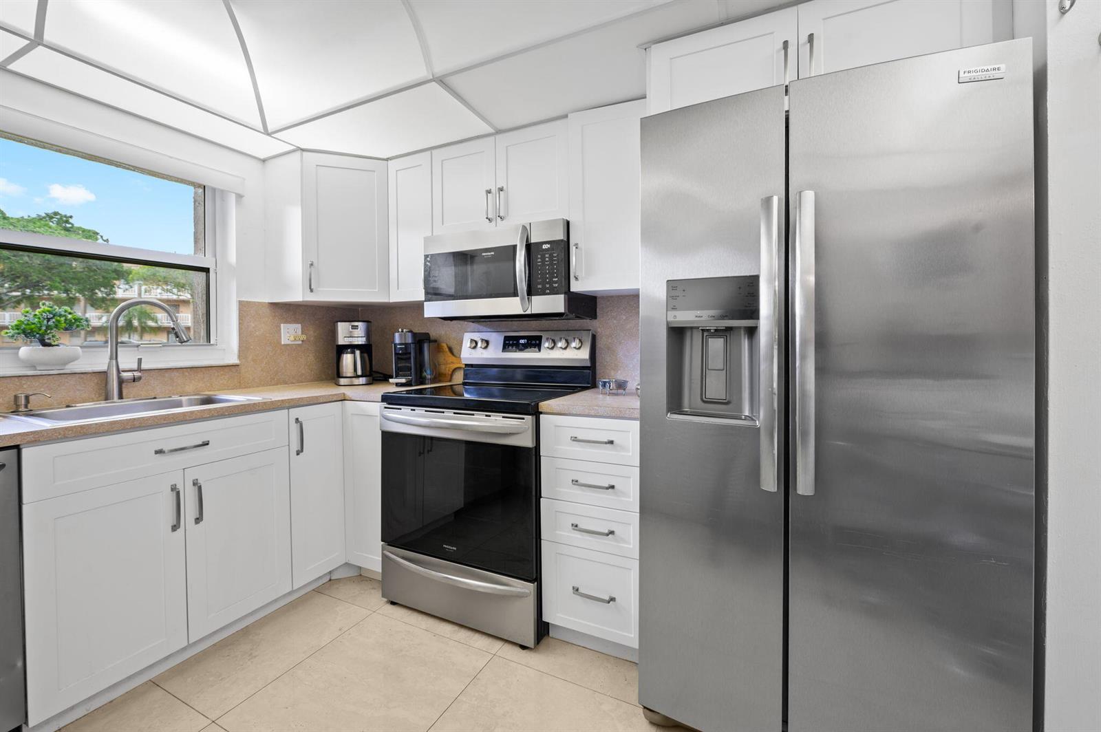 A kitchen with white cabinets, stainless steel appliances, a beige countertop, and a window view — 9330 E Sunrise Lakes Boulevard E # 104, Sunrise FL 33322, SUNRISE, FL