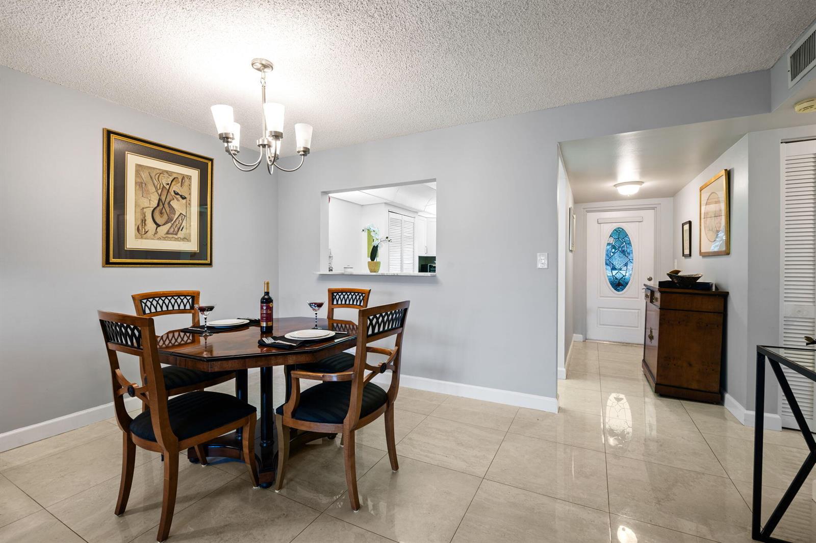 A dining room with a wooden table, four chairs, a chandelier, and light tile flooring — 9330 E Sunrise Lakes Boulevard E # 104, Sunrise FL 33322, SUNRISE, FL