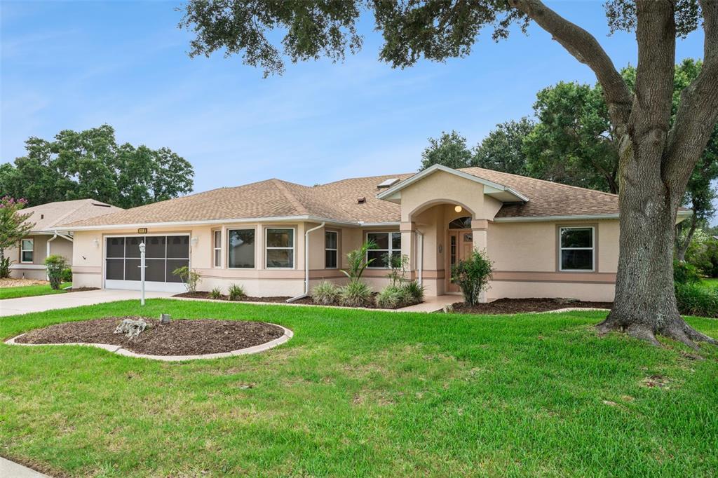 A single-story house with a tan stucco exterior, a shingled roof, and a large tree — 6441 WILANDER STREET, LEESBURG, FL