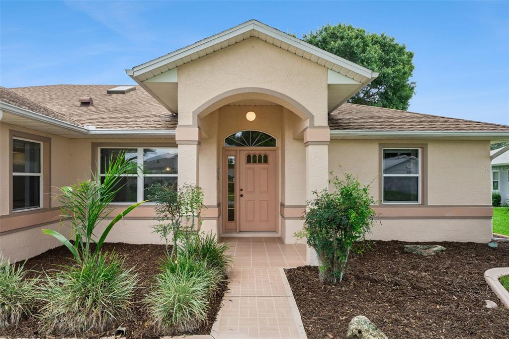 The exterior of a single-story house features a tan stucco facade, arched entryway, and walkway — 6441 WILANDER STREET, LEESBURG, FL