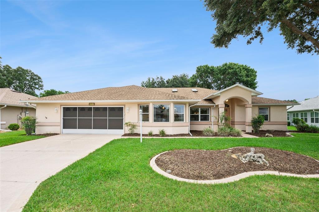 A single-story house with a tan stucco exterior, a two-car garage, and a landscaped lawn — 6441 WILANDER STREET, LEESBURG, FL