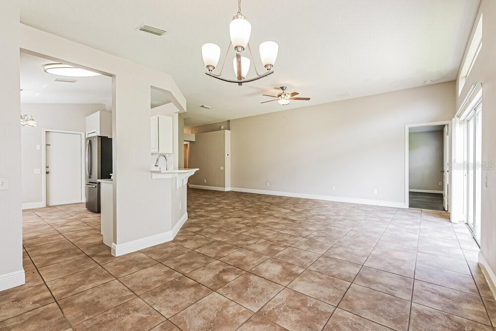 An open-concept living and dining area features neutral walls, tile flooring, and a chandelier — 10428 HUNTERS HAVEN BOULEVARD, RIVERVIEW, FL